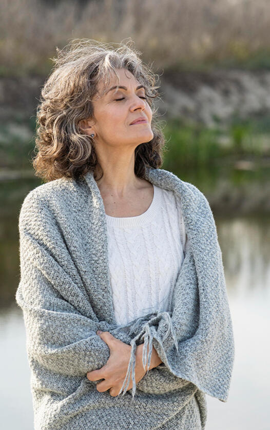 Woman, present in the moment, by a lake, wrapped in a blanket